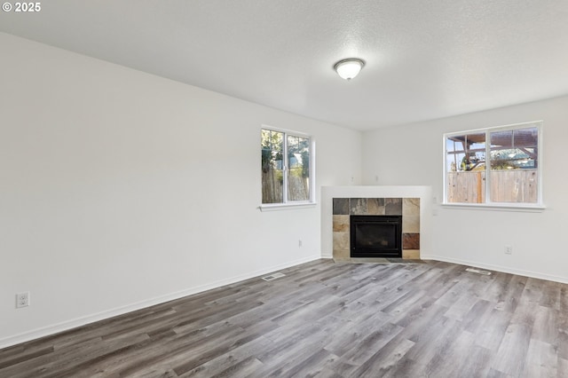 unfurnished living room with a tile fireplace, light wood-type flooring, and a textured ceiling