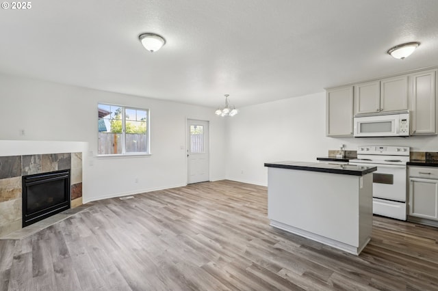 kitchen with white appliances, decorative light fixtures, a chandelier, light wood-type flooring, and a tiled fireplace