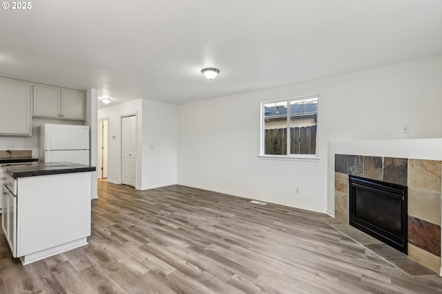 kitchen featuring white refrigerator, light wood-type flooring, and a tiled fireplace