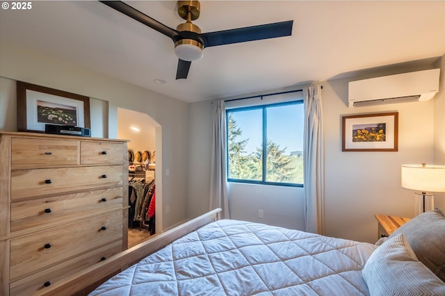 bedroom featuring arched walkways, a wall mounted air conditioner, a closet, ceiling fan, and a walk in closet