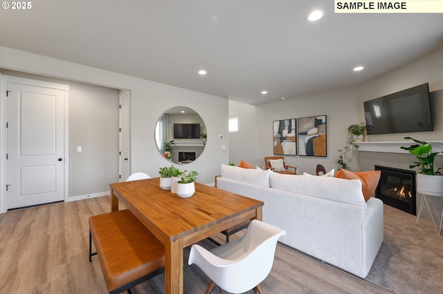 living room featuring a glass covered fireplace, recessed lighting, light wood-style floors, and baseboards