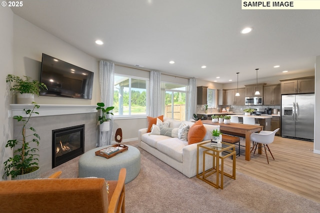 living area with recessed lighting, baseboards, light wood-style floors, and a glass covered fireplace