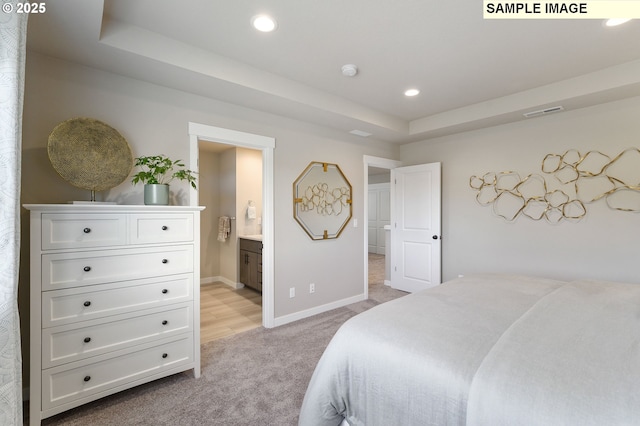 bedroom featuring light carpet, baseboards, a tray ceiling, recessed lighting, and ensuite bathroom