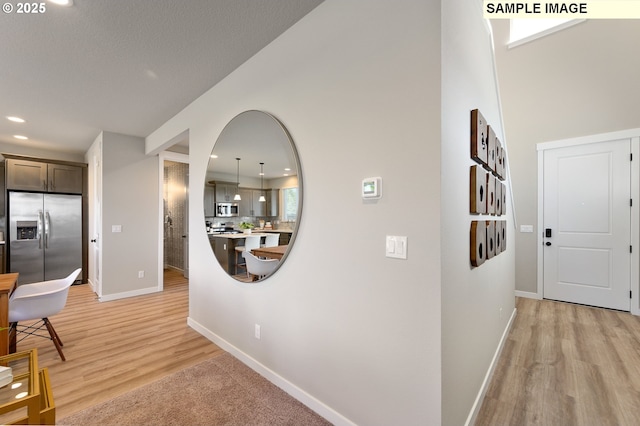 hallway featuring baseboards, light wood-style flooring, recessed lighting, and a high ceiling