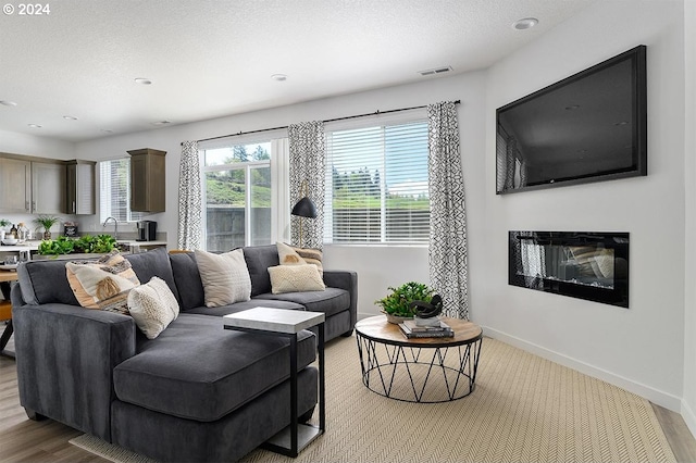 living area featuring a textured ceiling, visible vents, light wood-style floors, baseboards, and a glass covered fireplace