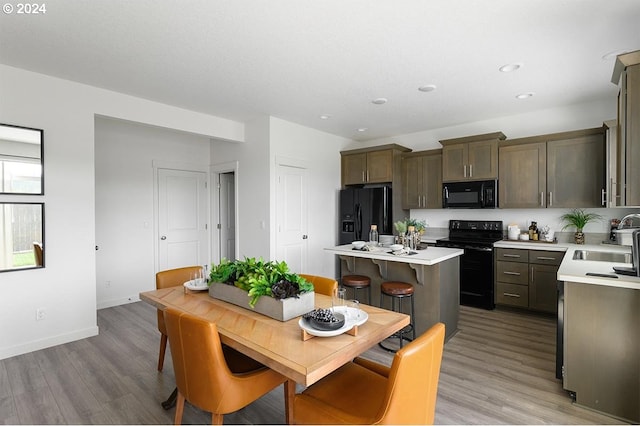 kitchen with a center island, light wood finished floors, light countertops, a sink, and black appliances