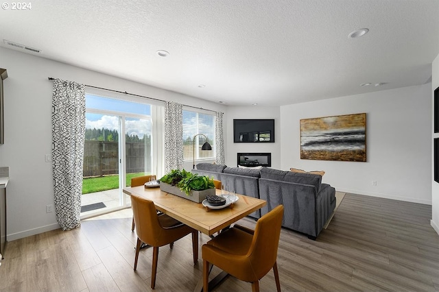 dining area with a glass covered fireplace, a textured ceiling, baseboards, and wood finished floors