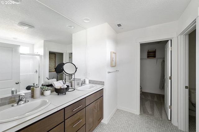 bathroom featuring a textured ceiling, a sink, a walk in closet, and a shower stall