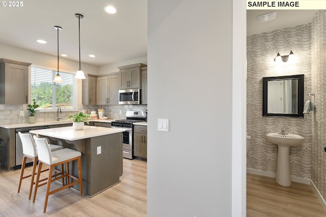 kitchen featuring stainless steel appliances, light wood-type flooring, light countertops, a breakfast bar, and wallpapered walls