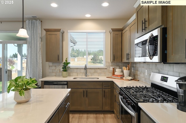 kitchen with stainless steel appliances, a sink, light countertops, light wood finished floors, and decorative light fixtures