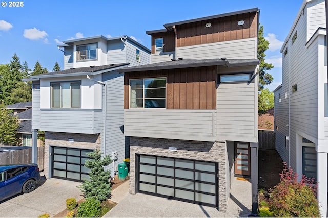 modern home with a garage, concrete driveway, stone siding, fence, and board and batten siding