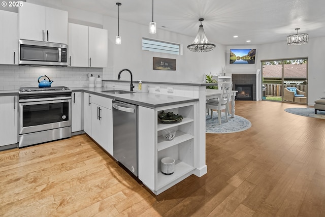 kitchen with a peninsula, a sink, open floor plan, appliances with stainless steel finishes, and dark countertops