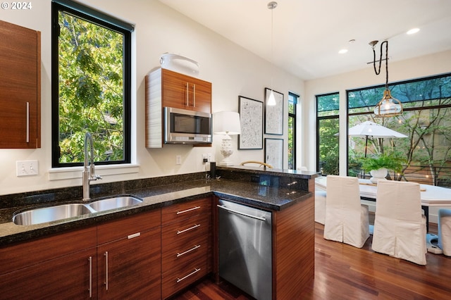 kitchen featuring sink, dark stone countertops, appliances with stainless steel finishes, pendant lighting, and a healthy amount of sunlight