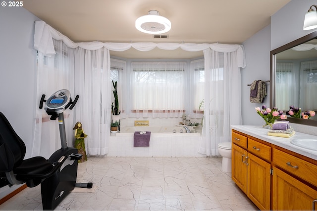 bathroom featuring vanity, tiled tub, and toilet