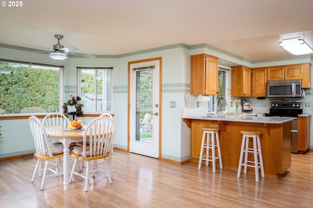 kitchen with stainless steel appliances, ceiling fan, light wood-type flooring, and kitchen peninsula