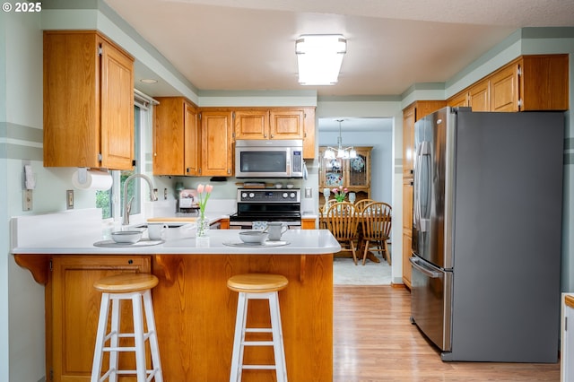 kitchen with a breakfast bar, stainless steel appliances, a notable chandelier, light hardwood / wood-style floors, and kitchen peninsula