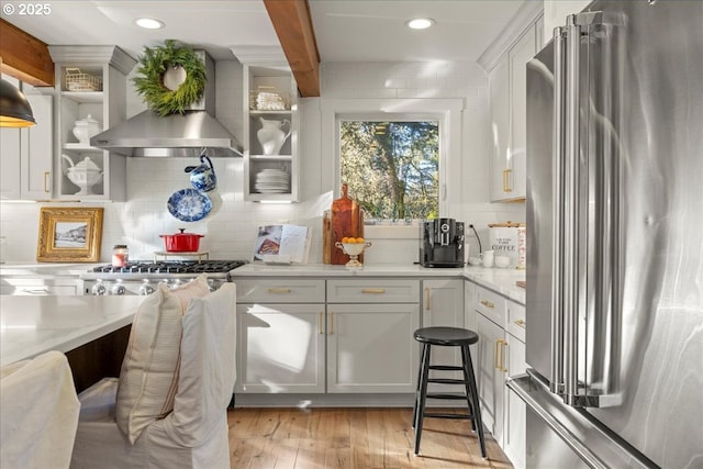 kitchen with white cabinetry, high end refrigerator, beamed ceiling, and wall chimney exhaust hood