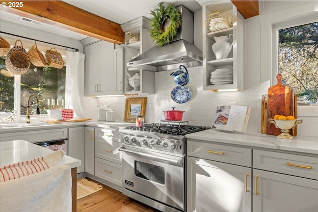 kitchen featuring light stone countertops, decorative backsplash, high end stainless steel range oven, wall chimney range hood, and beam ceiling