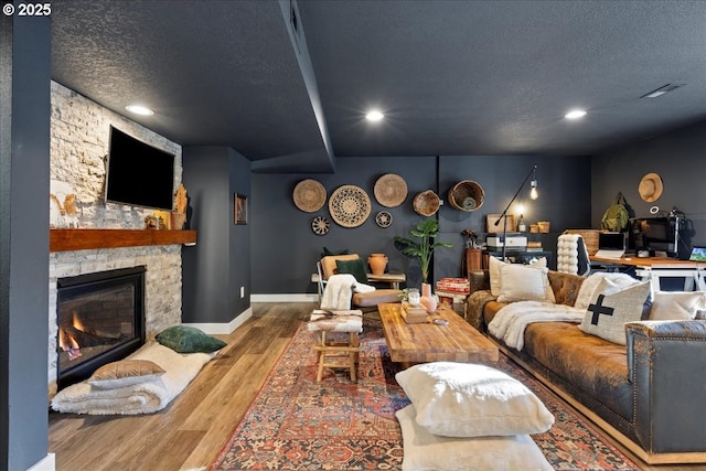 living room with hardwood / wood-style floors, a stone fireplace, and a textured ceiling