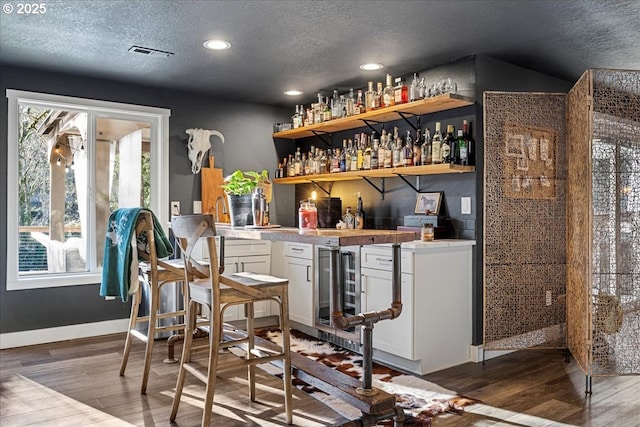 bar with white cabinets, dark wood-type flooring, and a textured ceiling