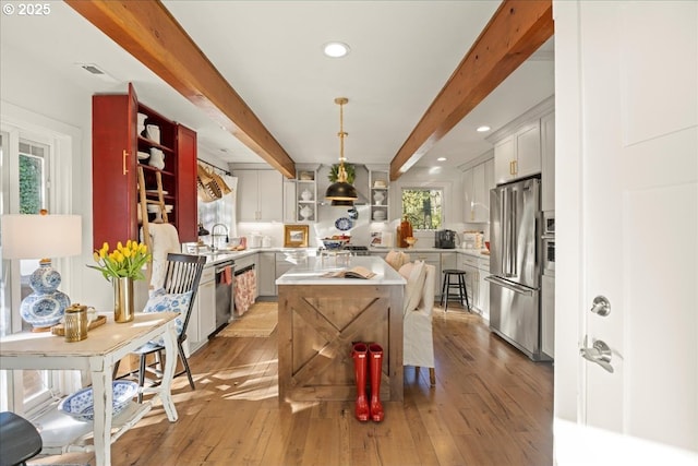 kitchen with appliances with stainless steel finishes, beamed ceiling, hardwood / wood-style floors, white cabinetry, and hanging light fixtures