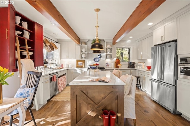 kitchen featuring white cabinets, hanging light fixtures, light wood-type flooring, appliances with stainless steel finishes, and beamed ceiling