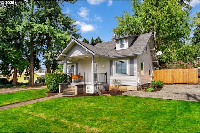 view of front facade with covered porch, a front yard, fence, a chimney, and a shingled roof