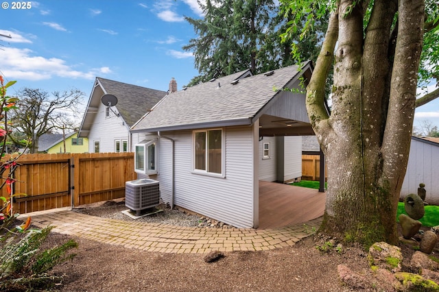 rear view of property featuring a gate, fence, a shingled roof, and central air condition unit