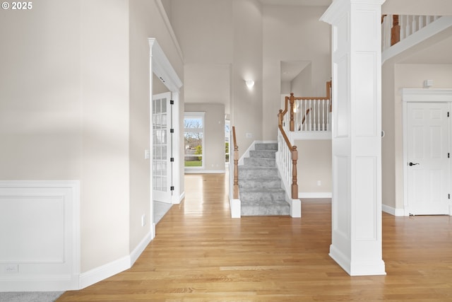 foyer entrance featuring stairs, ornate columns, light wood-type flooring, and baseboards