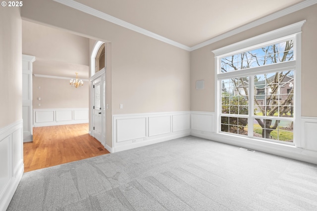 unfurnished room with a chandelier, wainscoting, ornamental molding, and carpet floors