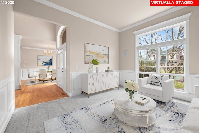 living area featuring a wainscoted wall, ornamental molding, a decorative wall, and a notable chandelier