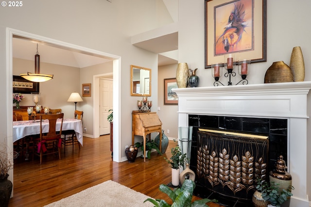 living area featuring a fireplace with raised hearth, baseboards, and wood finished floors