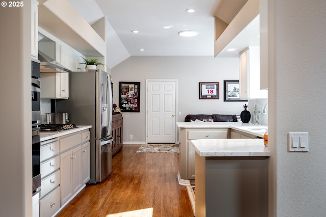 kitchen featuring white cabinets, appliances with stainless steel finishes, wood finished floors, a peninsula, and a sink