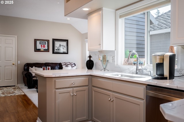 kitchen featuring a peninsula, wood finished floors, a sink, stainless steel dishwasher, and light stone countertops