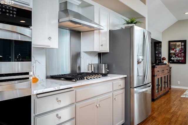 kitchen with wood finished floors, white cabinets, appliances with stainless steel finishes, backsplash, and wall chimney exhaust hood