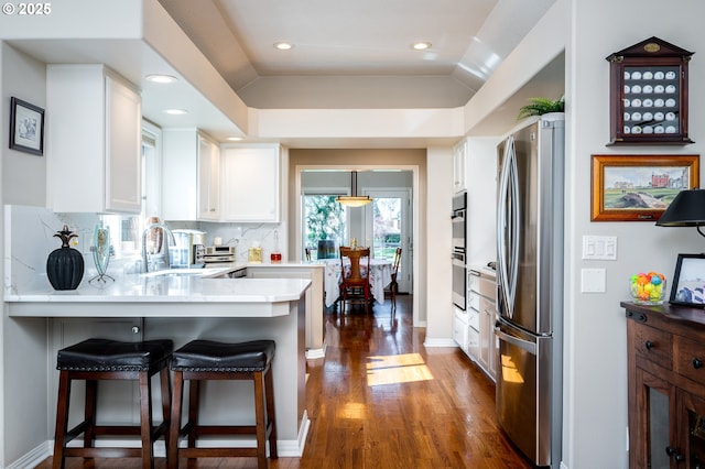 kitchen featuring a peninsula, dark wood-style flooring, a sink, white cabinets, and appliances with stainless steel finishes