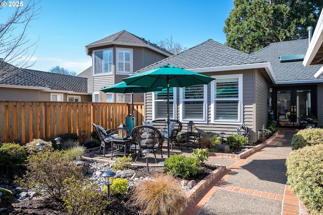 rear view of house with roof with shingles, a patio area, and fence