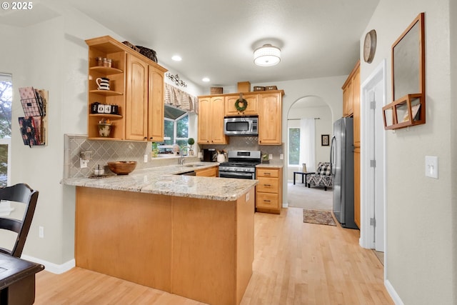 kitchen featuring sink, stainless steel appliances, decorative backsplash, kitchen peninsula, and light wood-type flooring