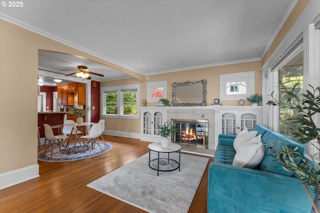 7406 N Fiske Ave, Portland, OR 97203 - living room with wood finished floors, ornamental molding, a tiled fireplace, a ceiling fan, and a textured ceiling
