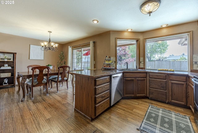 kitchen featuring dark countertops, wood finished floors, dishwasher, a sink, and an inviting chandelier