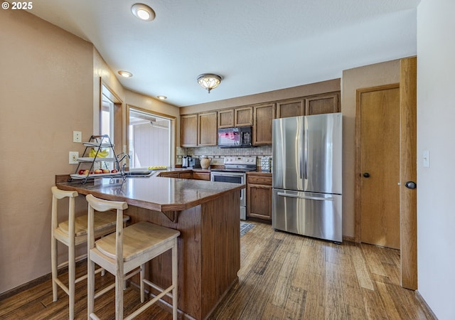 kitchen featuring a peninsula, wood finished floors, a kitchen bar, and stainless steel appliances