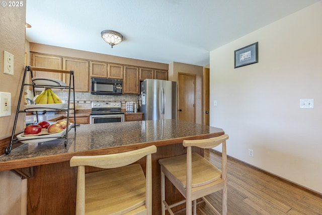 kitchen with stainless steel appliances, dark countertops, a kitchen breakfast bar, and light wood-style floors