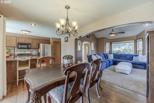 dining room with light wood-style floors, arched walkways, and ceiling fan with notable chandelier
