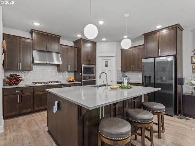 4745 S 19th St, Ridgefield, WA 98642 - kitchen with light wood-type flooring, dark brown cabinets, a sink, under cabinet range hood, and stainless steel appliances