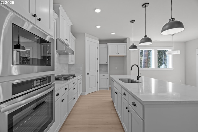 kitchen with appliances with stainless steel finishes, white cabinetry, sink, hanging light fixtures, and a kitchen island with sink