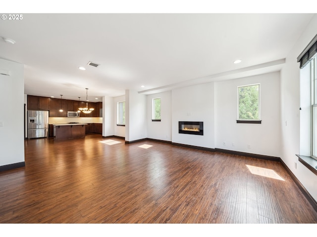 unfurnished living room featuring visible vents, dark wood-type flooring, a notable chandelier, and a healthy amount of sunlight