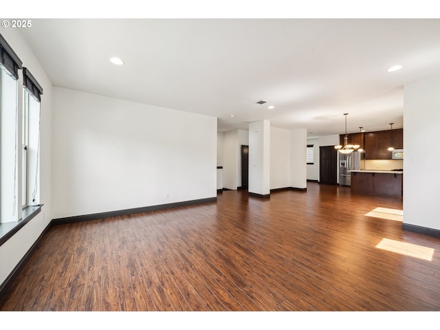 unfurnished living room with recessed lighting, baseboards, an inviting chandelier, and dark wood-style floors