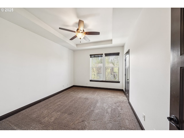 carpeted empty room featuring baseboards, ceiling fan, and a tray ceiling