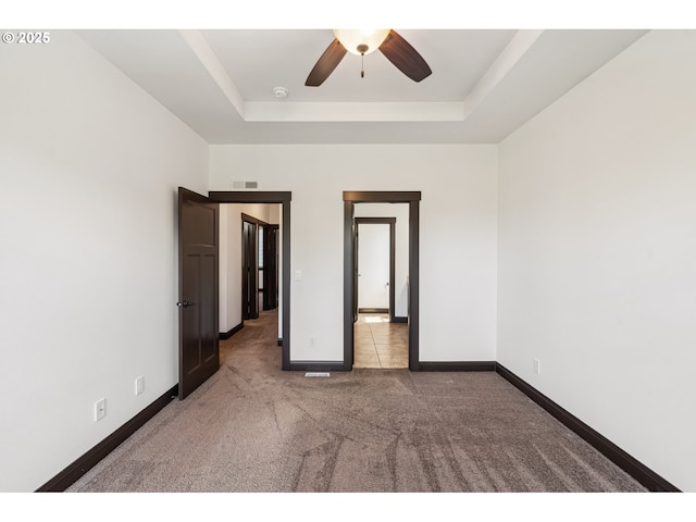 empty room with visible vents, baseboards, ceiling fan, a raised ceiling, and carpet