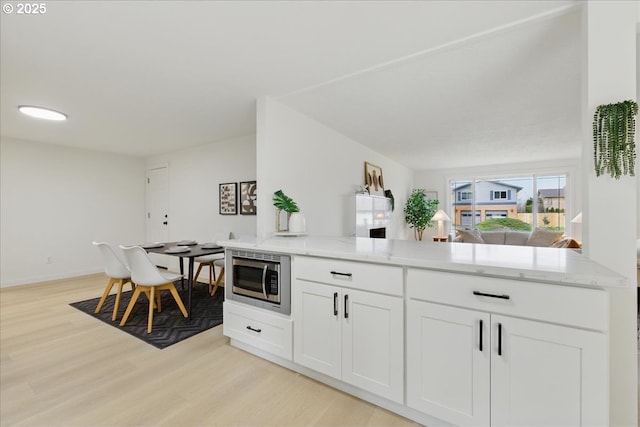 kitchen featuring stainless steel microwave, light stone counters, light hardwood / wood-style flooring, and white cabinets